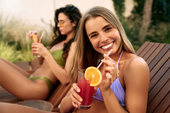 Smiling woman holding orange slice while relaxing with friend and drinking juice outdoors