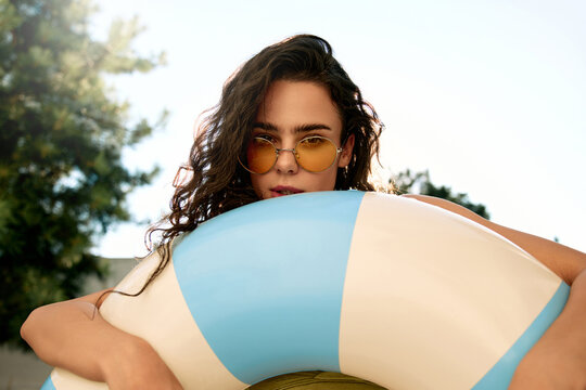 Young woman in green bikini posing with inflatable ring at poolside on summer day - Powered by Adobe