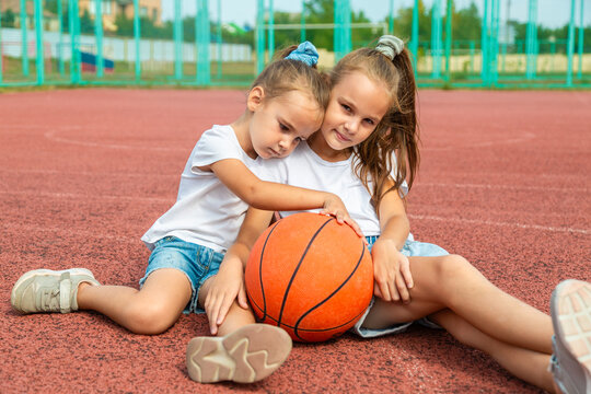 Friends children taking a break from training on a basketball court. Two sisters playing a ball together