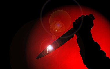 silhouette of scary hand with knife in red spotlight in the darkness.