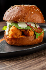 Gourmet fried chicken sandwich with sesame bun, crispy fillet, fresh greens, pickled onions, and herb sauce on black plate. Vibrant colors and textures, ideal for food photography.