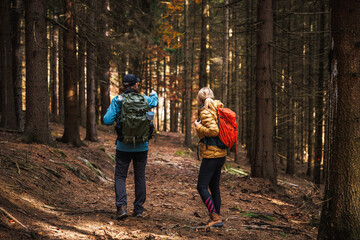 Two friends wearing sport clothing walking on trekking trail in woodland. Tourist hiking in autumn forest
