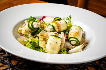 Zucchini rolls with cheese atop vibrant greens create a delightful dish at a lively venue