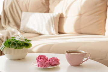 Pink flower marshmallows and tea on a coffee table with a cozy couch. Soft focus