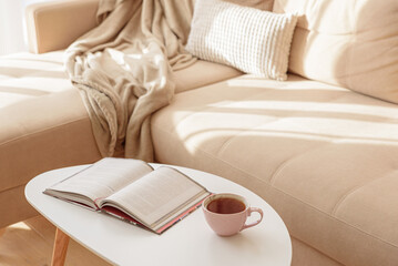 Cozy living room with a book and tea on a beige couch. Soft focus