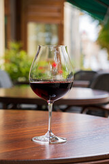 A glass of deep red wine on a polished table, surrounded by lush greenery, invites relaxation
