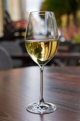 Sunlight glimmers on a glass of white wine, set on a rich wooden table in a charming cafe