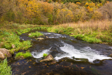 A River In A Meadow Bordered By Woods During Autumn 