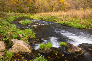 A River In A Meadow Bordered By Woods During Autumn 