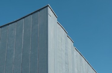 Fototapeta premium Modern building with gray metal panels against clear blue sky. Architectural facade detail features clean lines and geometric shapes. Industrial design showcases contemporary construction.