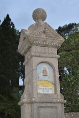 Obraz premium Stone monument at the Santuari de la Mare de Déu de Bonany near Petra, Mallorca, adorned with a hand-painted ceramic tile depicting Marian imagery and surrounded by lush greenery 