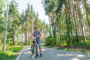 Obraz premium Young father with his little daughter on bicycle in summer sunny forest