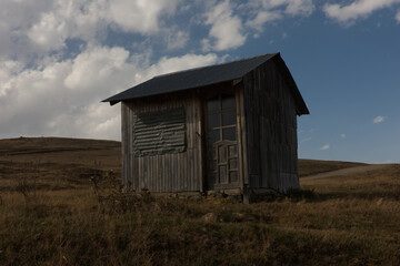Obraz premium Two photos of a rustic wooden shed situated in a rugged natural landscape with cloudy and dynamic skies. These images capture the textures of weathered wood, the earthy tones of dry grass, and a moody