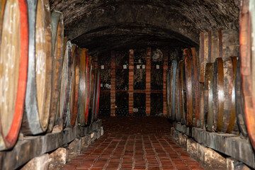 Dark cellar with old bottles of wine. Process of wine maturation in bottles on wooden racks in wine vault.
Aged traditional wooden vine barrels lined up in cool and dark vine cellar