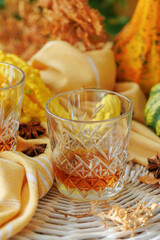 Whiskey glass on woven table with warm-toned fabric, yellow gourd, and autumn-themed decorations