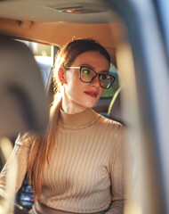 Young businesswoman sits inside car and looks at her partner, in warm sunlight