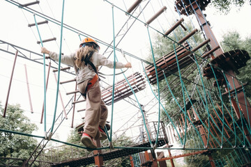 Young child wearing safety harness and helmet skillfully navigates a challenging high rope course. Surrounded by trees, this outdoor adventure highlights courage and balance.