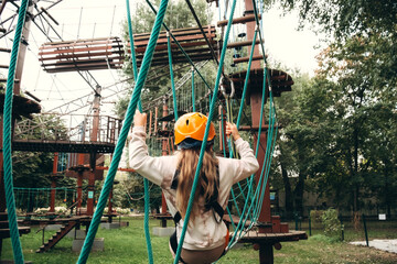 Young child wearing safety gear makes their way across a challenging ropes course in an adventure park. The image captures focus and determination during this outdoor activity amid lush surroundings.