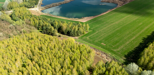 Aerial view of green fields and a serene pond surrounded by lush trees, showcasing the beauty of nature during springtime in a rural landscape.