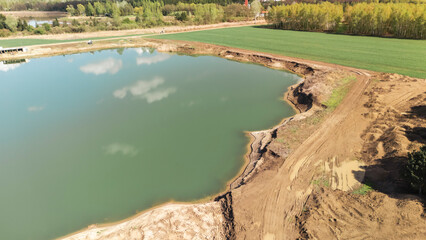 Aerial view of a tranquil water body surrounded by lush greenery and farmland. The scene captures the harmony of nature and agriculture in a serene environment.
