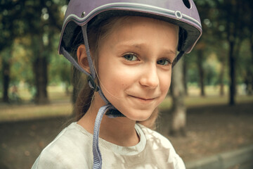 Child wearing a protective helmet with a gentle smile on their face, standing outside in a park setting. Capturing an expression of safety, happiness, and outdoor adventure.