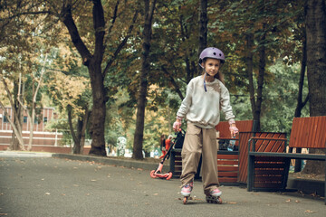 Young child rollerblading through a tree-lined park wearing a helmet for safety. The setting is serene, with benches and scattered leaves, capturing an active, joyful moment.
