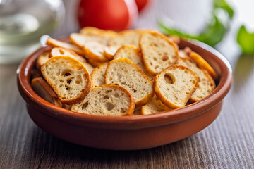 Crispy roasted bruschetta bread in bowl on wooden table.