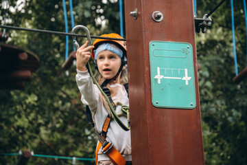 Young child enjoys an outdoor adventure park, confidently climbing while wearing safety gear. The setting is surrounded by lush greenery, highlighting the joy of outdoor activities.