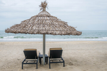 Pair of deck chairs under a palm umbrella in beautiful Cua Dai Beach in Hoi An, Central Vietnam