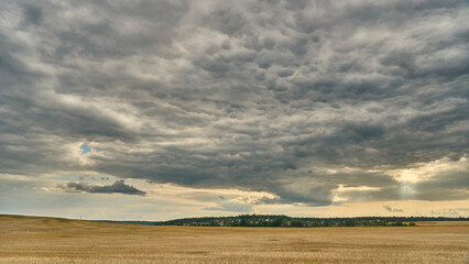 clouds over an agricultural field. A spring landscape with a forest, an empty field and clouds. A field after harvesting wheat.