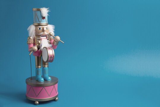 Festive Holiday Decoration. A whimsical nutcracker drummer, dressed in a vibrant contemporary palette of pink and gold, captures the joyful spirit of the season. Set against a bold blue background
