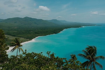 Vibrant turquoise waters meet lush green hills and a sandy beach, showcasing tropical paradise.