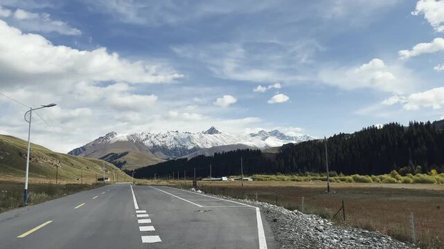 car traveling on road leading to snow mountain in xinjiang, china