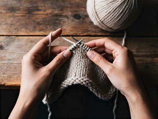 Hands knitting with thick cream wool yarn in soft daylight on rustic wooden table