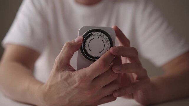 Close-up cropped shot of man setting mechanical timer switch, device used to control the on off cycles of electrical appliances, promoting energy efficiency and convenience in household management.