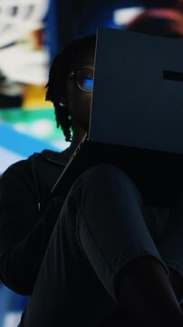 Vertical video Woman staring at laptop screen, feeling tired while doing homework. African american teenager struggling to stay focused while reading school books, battling fatigue and distractions