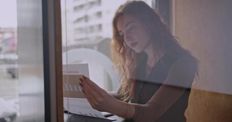 A young businesswoman reviews charts and graphs in a cafe. She is focused and determined, reflecting the challenges and rewards of entrepreneurship.