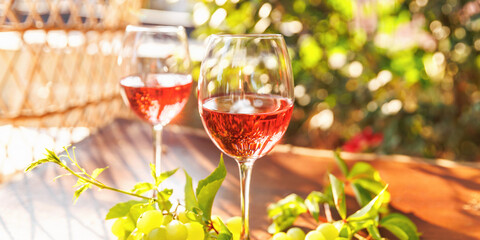 Closeup of rose wine glass with white grapes and vine leaves on sunlit terrace table outdoors