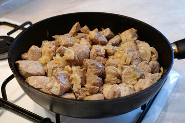 Frying meat. Pieces of meat with onion in frying pan on gas stove
