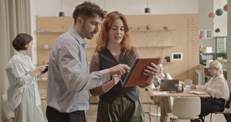 Multicultural business team collaborating on a project using a tablet in a modern office space. - Powered by Adobe