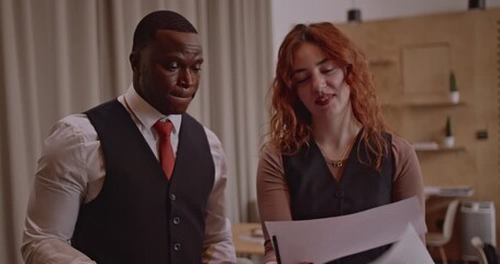 Multicultural business partners review charts and graphs together in their modern office. Diverse colleagues discuss their next business strategies for the future. - Powered by Adobe