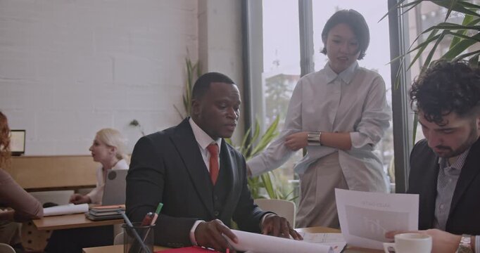 Diverse colleagues discuss analysis and brainstorm ideas in a co working space coffee bar. International team collaborates on a startup project, reviewing charts and data. - Powered by Adobe