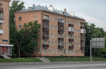Angled view of a brick apartment block with repetitive windows and enclosed balconies