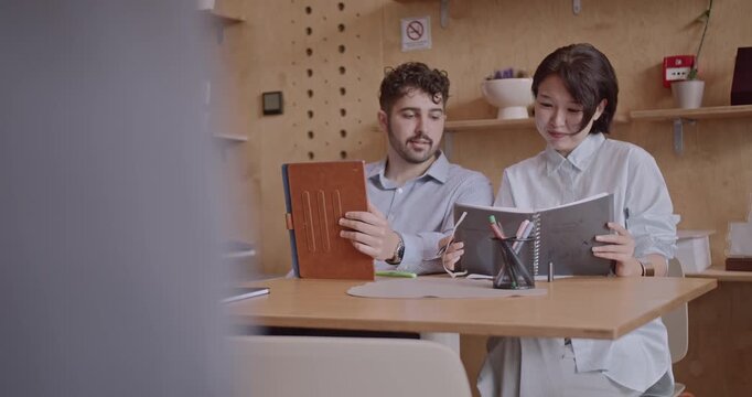 Two diverse colleagues collaborate on a project in a modern office, utilizing a tablet and notebook to analyze data and strategize. - Powered by Adobe