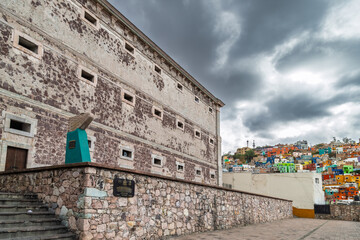 Obraz premium Stone facade of Museo Regional de Guanajuato Alhondiga de Granaditas with colorful hillside houses in background