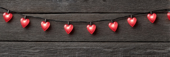 Romantic red heart shaped light garland hanging on dark rustic wood background. This lovely decoration creates festive, cozy, and warm atmosphere for celebration