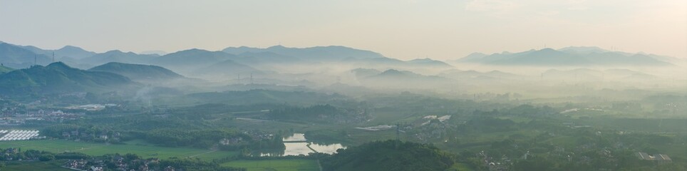 Lush Green Landscape with Mist and Distant Buildings at Dawn © Zelanya