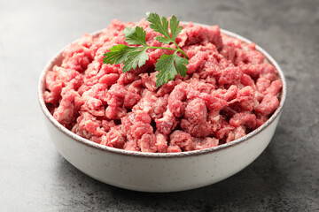 Raw minced meat with parsley on grey table, closeup