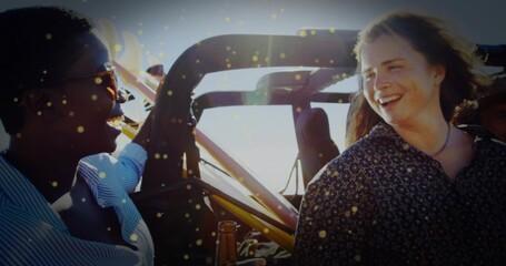 Laughing two women holding bottled drinks inside off-road vehicle in sunlight, with roll cage frame