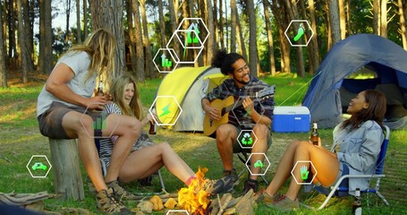 Friends playing guitar, holding beer bottles at campfire in forest clearing, with yellow or blue ten
